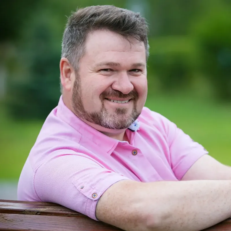 Smiling man in a pink shirt sitting on a park bench