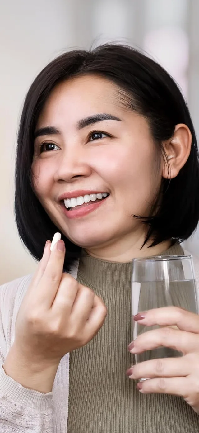 Woman smiling as she takes a capsule with a glass of water